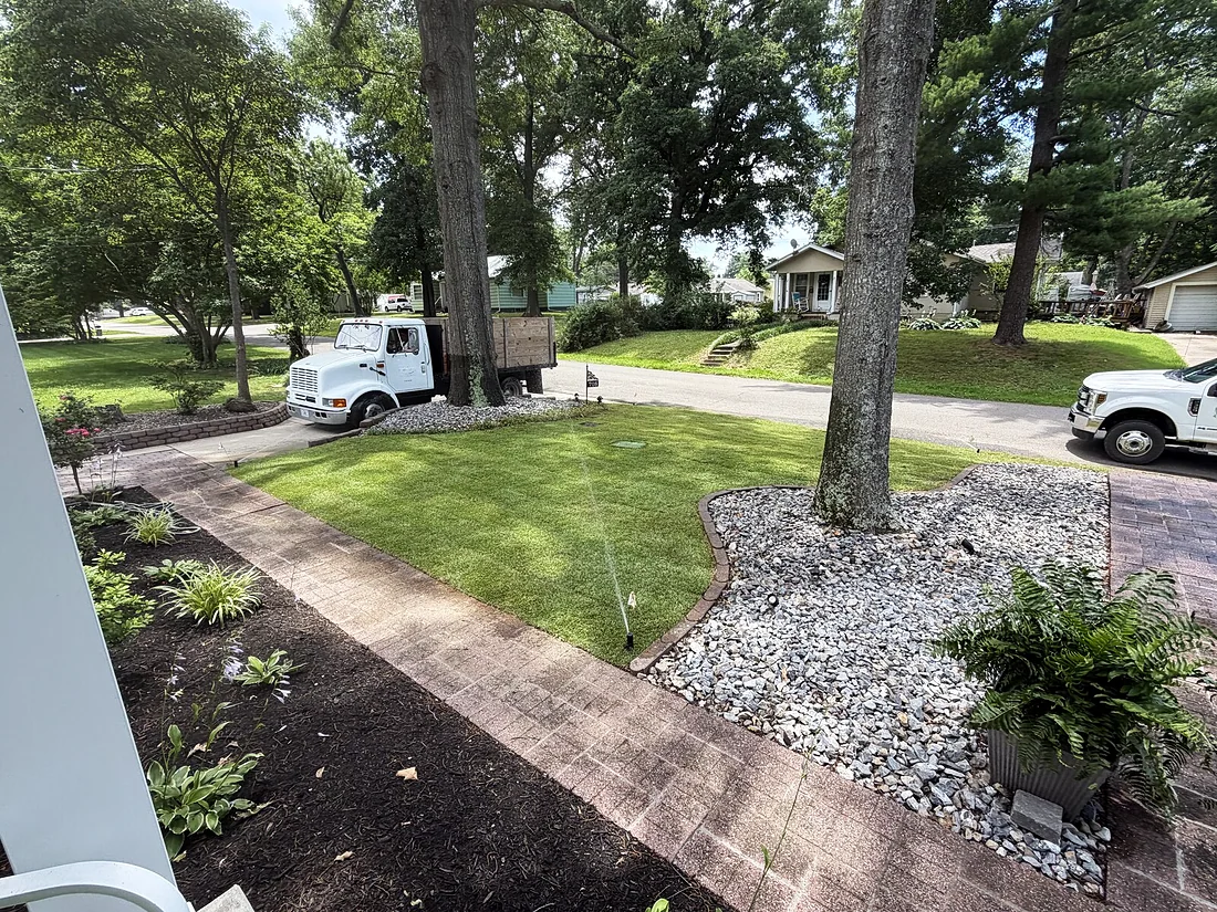 Irrigation system running on a newly sodded lawn beside a brick walkway